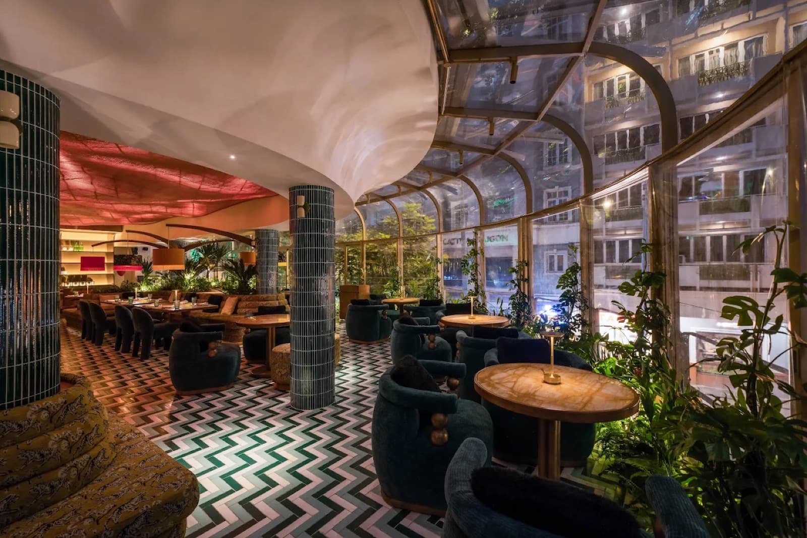 Yunka's glass-roofed conservatory dining and lounge area at night, empty, with the city visible through the glass.