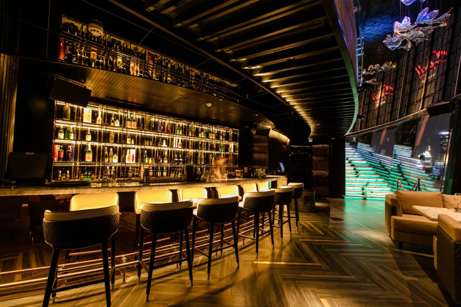 The indoor Lounge Area at Chill Skybar, unoccupied, showing its illuminated bar, high seating, sofas and staircase.