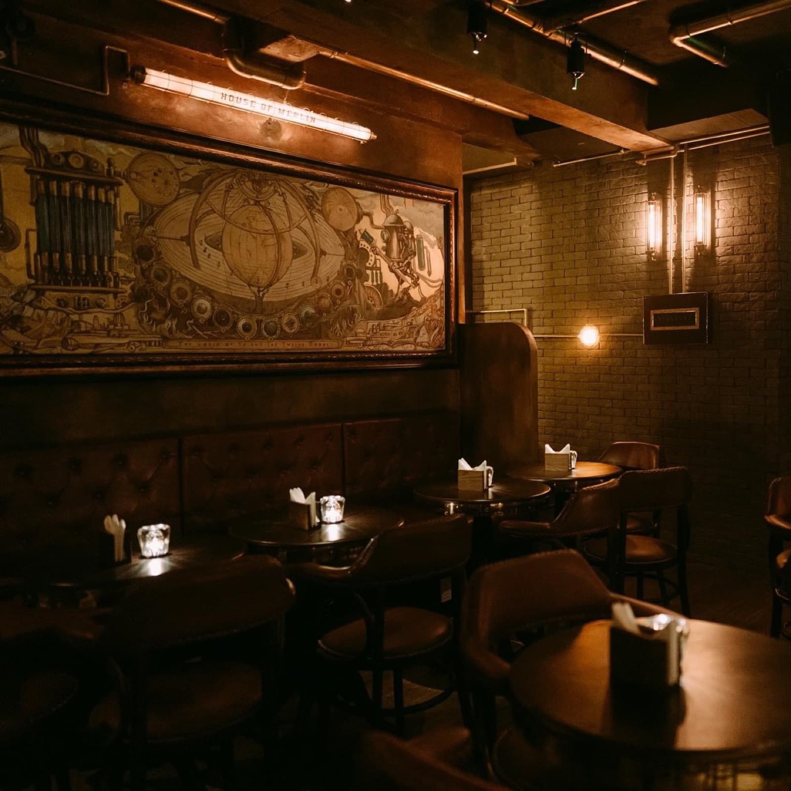 House of Merlin's main room, unoccupied, showing booth seating and the etched brass mural along the brick wall.