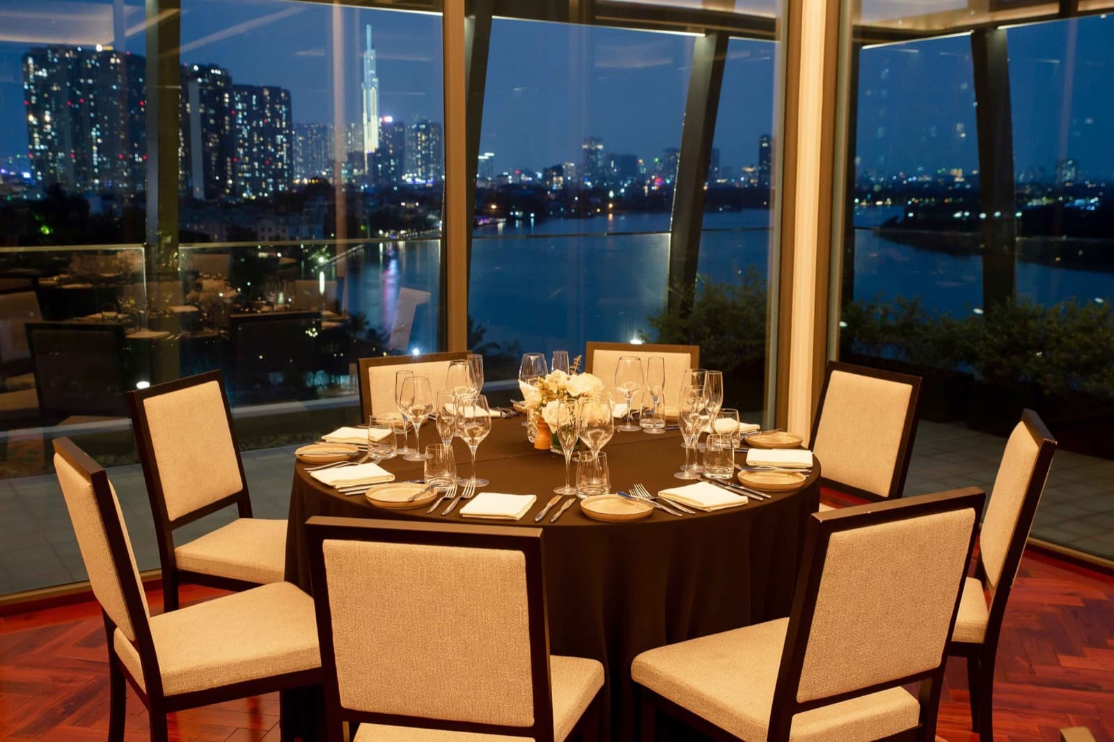 The Emerald room at Mia Saigon set with a round table, unoccupied, with the river and city lights through the glazing.