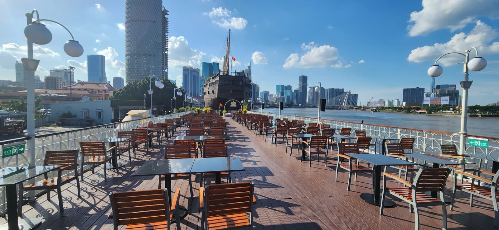 Wide, unoccupied Sundeck view with river, skyline, tables and the Saigon Princess entrance arch