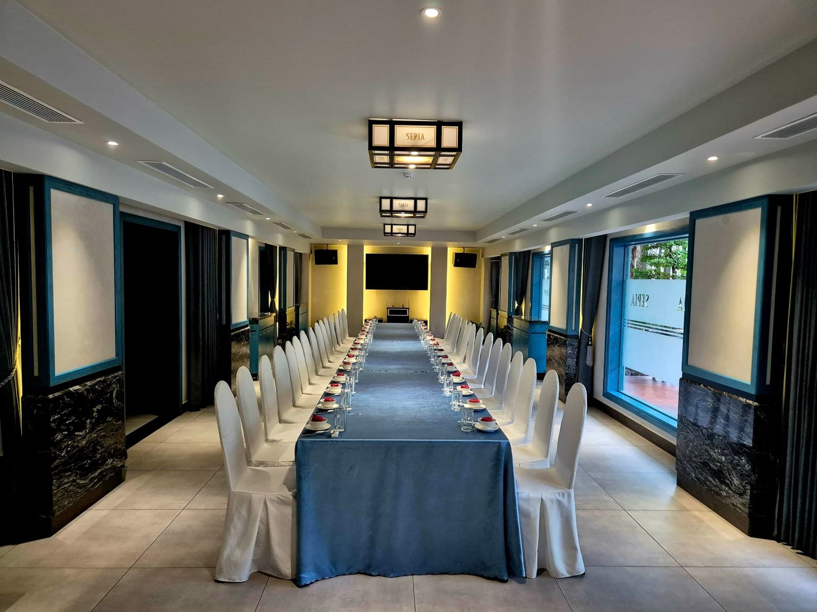 Blue-accented private dining room arranged with a long table and white-covered chairs