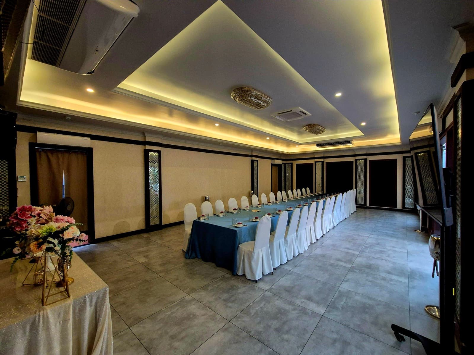 Cream-toned private dining room arranged with a long table and white-covered chairs